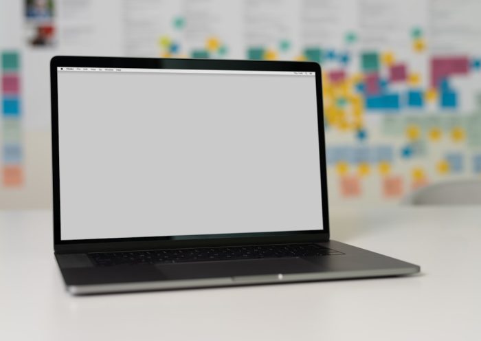 A laptop on a table with a blurred background of colorful sticky notes and charts