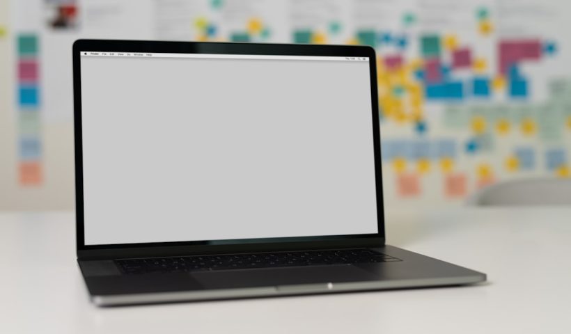 A laptop on a table with a blurred background of colorful sticky notes and charts