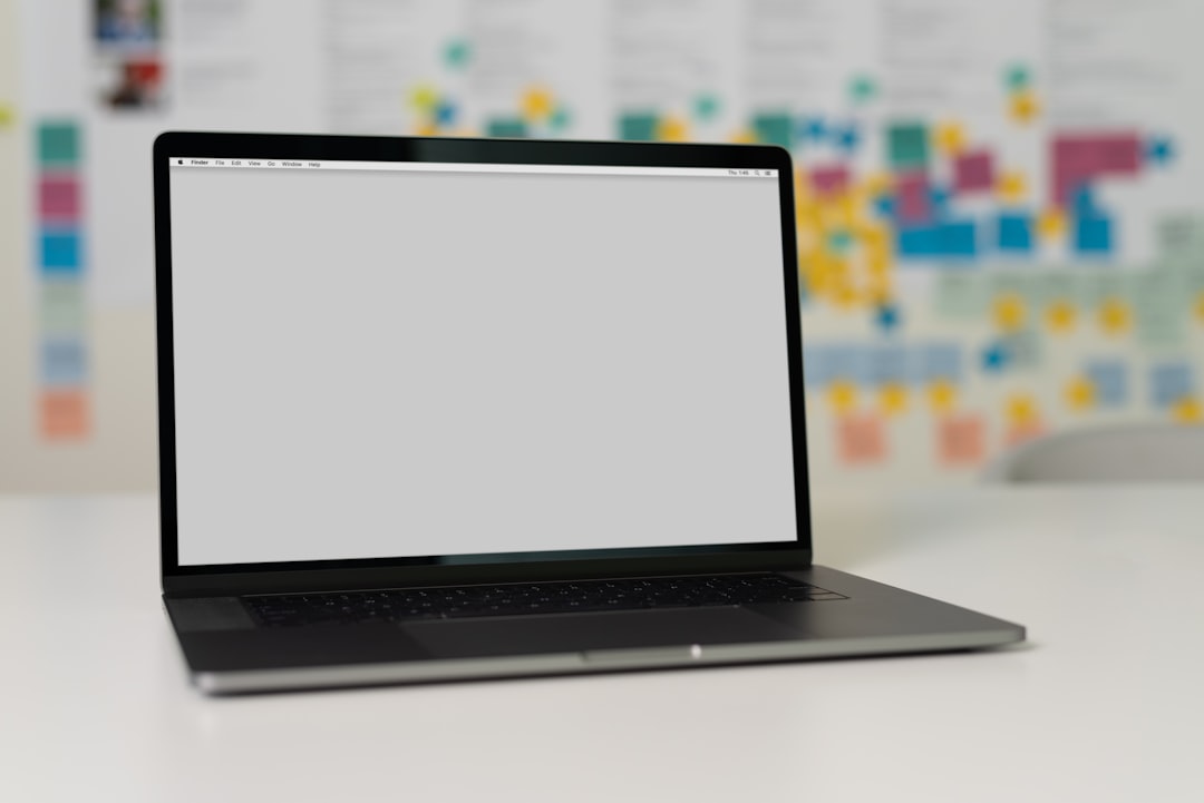 A laptop on a table with a blurred background of colorful sticky notes and charts